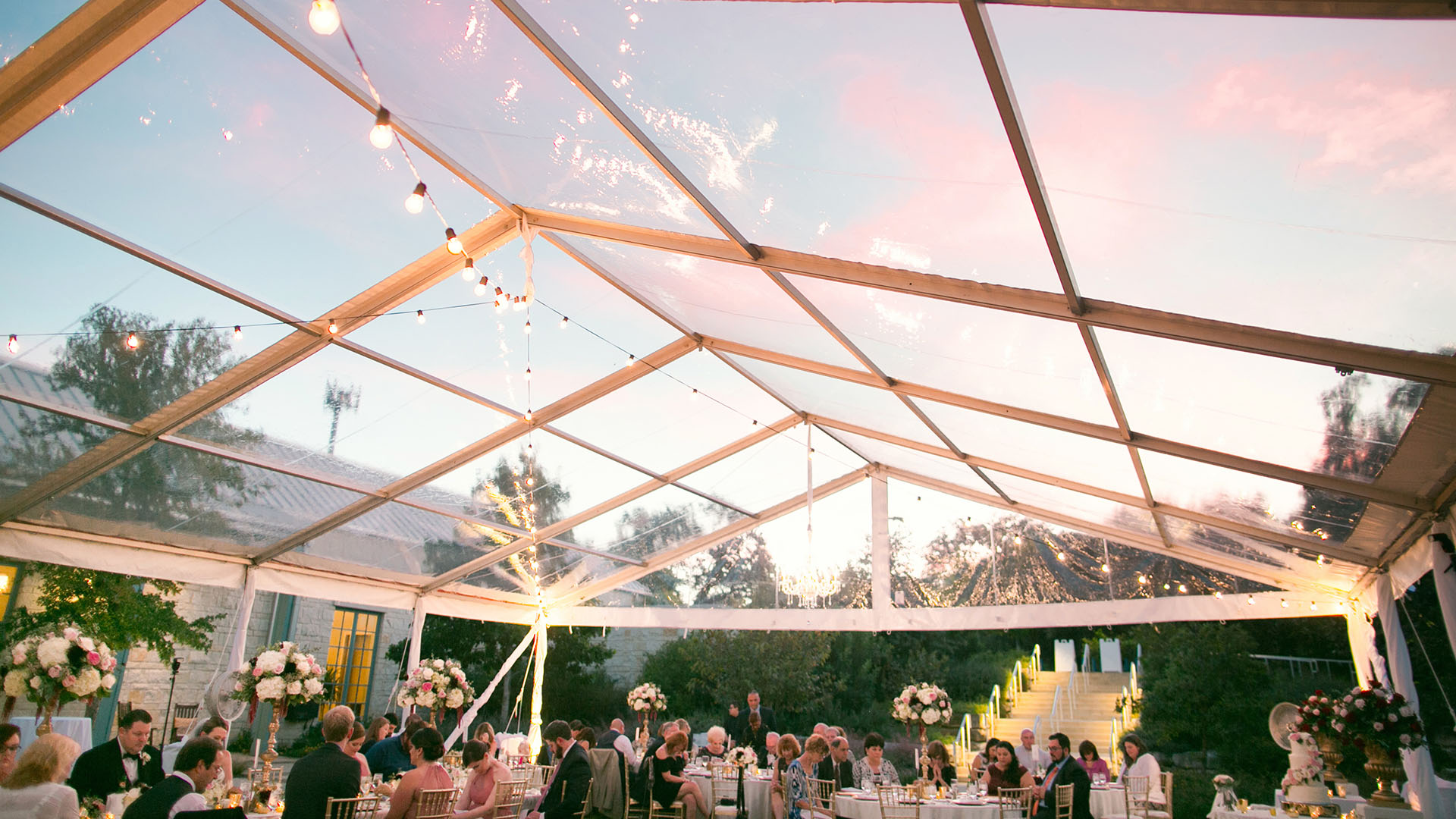 Large tent with clear roof, string lights underneath, wedding attendees underneath with decor