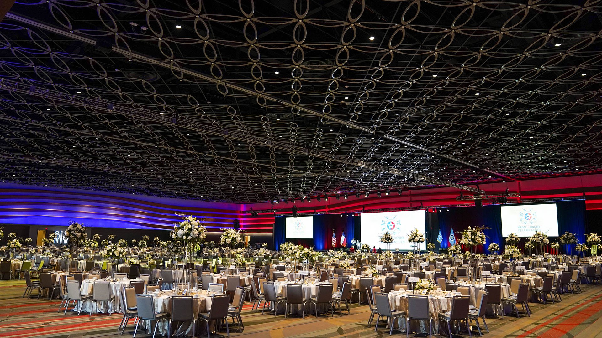 Large building set up for reception, stage in front of lots of tables decorated accordingly
