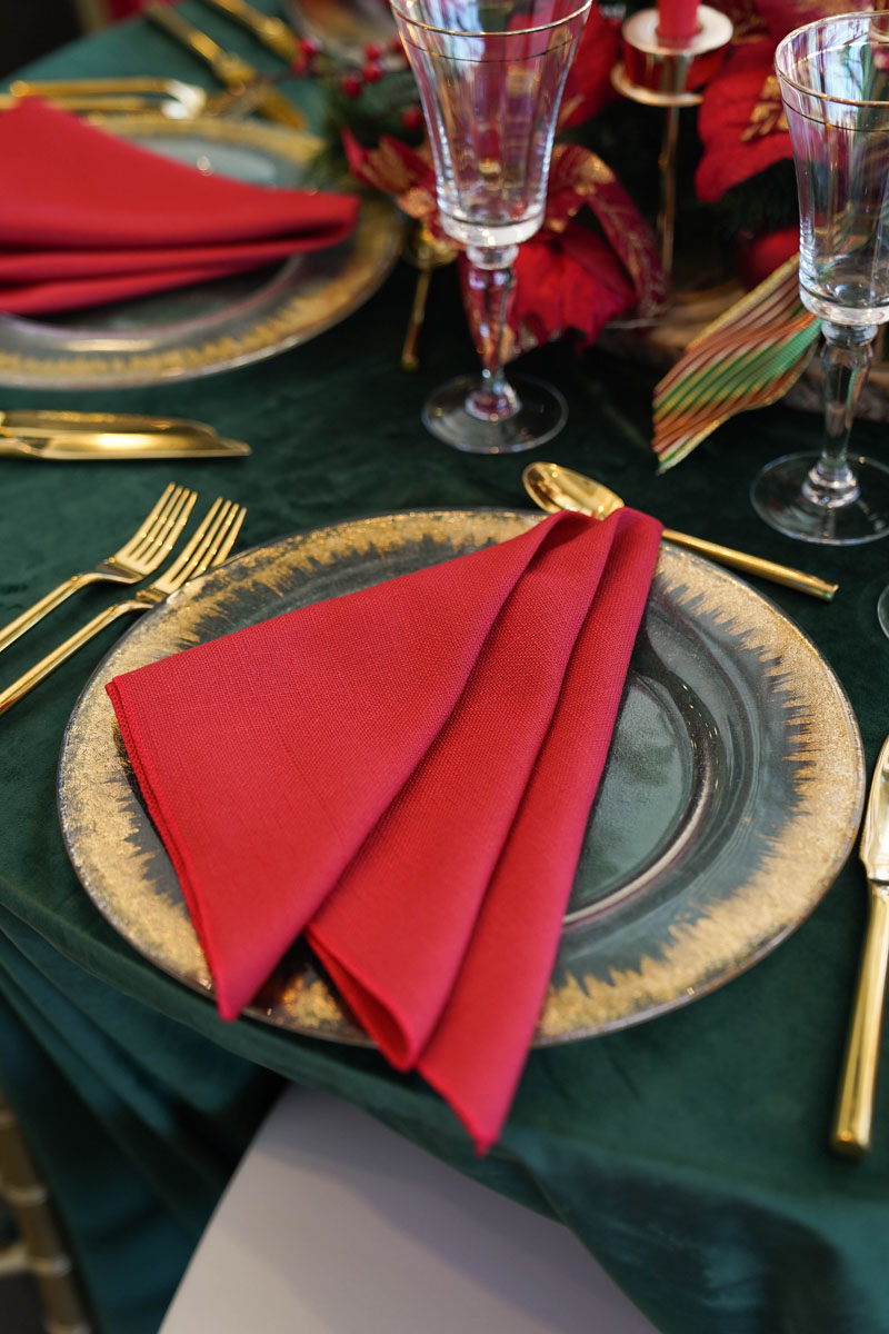 A table setting featuring elegant red napkins and ornate gold plates, creating a festive and sophisticated dining atmosphere.